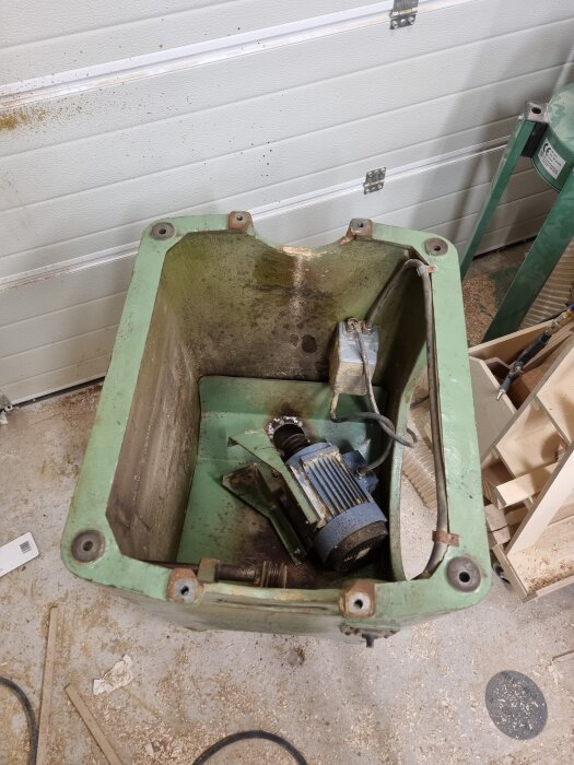 Grön sågkropp med borttagen motor och kablar, inuti ett garage.