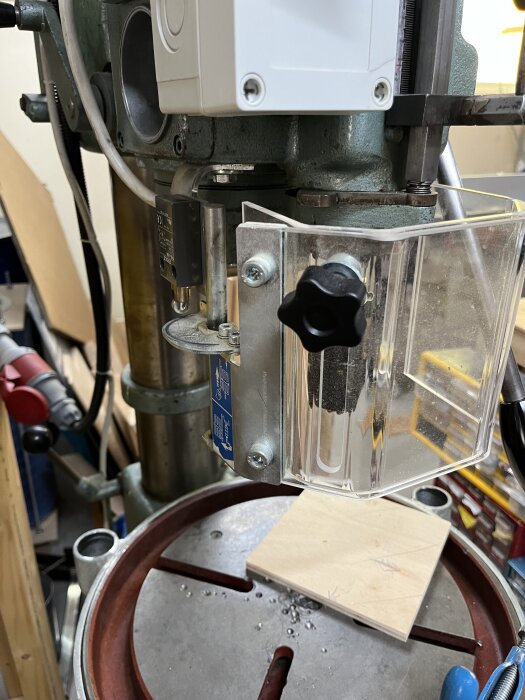 Bilden visar ett chuckskydd monterat på en pelarborrmaskin med en träbit på maskinens bord.