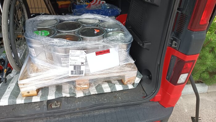 En lastpall med burkar av linoljefärg från Ottossons Färgmakeri i bakluckan på en röd bil, i samband med ett målningsprojekt.