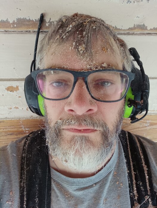 Person med dammig tröja och skyddsglasögon arbetar på träpanel.