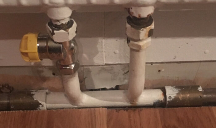 Radiatorventil med vitmålade rör och gul justeringsdel, visar möjlig installation av strypning och bypass i ett värmesystem.