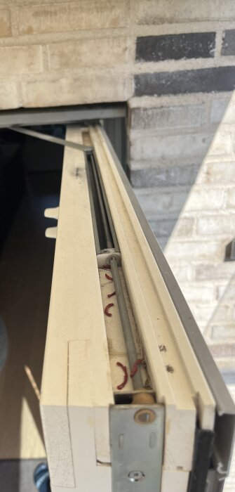 Altandörr med trasig fönsterbroms och stång som går ut på höger sida, visar detaljer av handtag och bromshus i närbild.