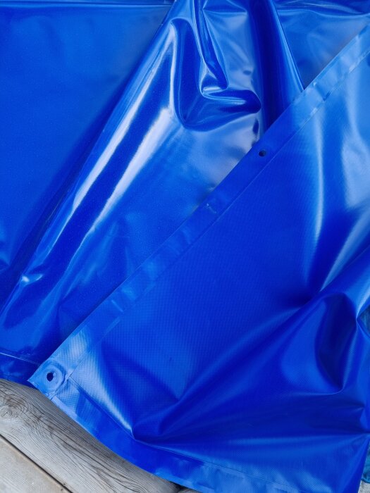 Blått poolskydd med gråa ringar på en träterrass.