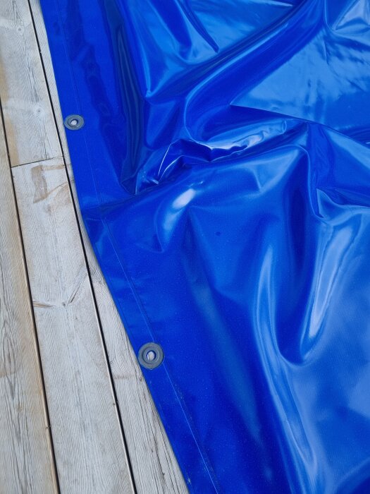 Blått poolskydd med metallring synlig längs kanten, liggande på träyta.