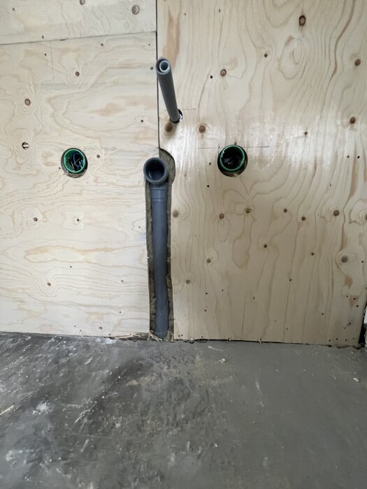 Vägg med rörinstallation i träpanel med två synliga rör och elektriska kopplingsdosor.