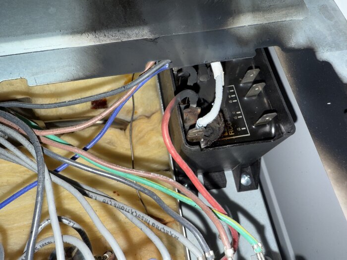 Elektrisk anslutning med trasiga kablar och en svart box bakom en Husqvarna ugn, visar tecken på elbrand.