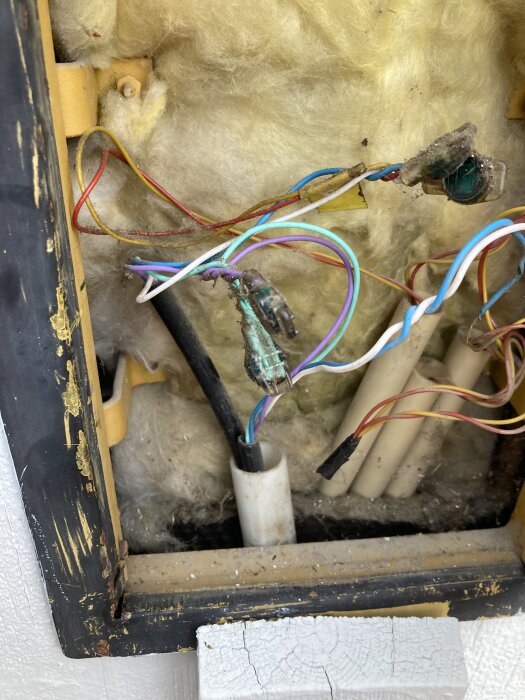 Plåtlåda på fasad med telekablar, olika färgade ledare skarvade ihop. Två svarta kablar syns, varav en går vidare, isolering i bakgrunden.