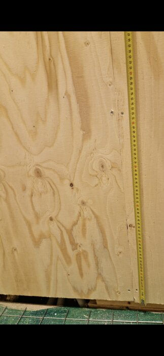 Plywoodvägg med få skruvar, mätband visar storlek; delar av duschhörna där fuktskada upptäckts runt Unidrain golvbrunn.