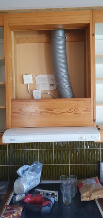 Köksfläkt med synlig frånluftskanal och styrdon ovanför; verktyg och material på bänkskiva bredvid.
