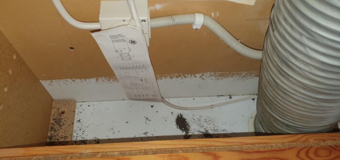Styrdon med ritning, kopplat till ett flexibelt ventilationsrör och kablar, mot en trävägg i ett kök.