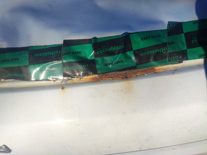 Grön och svart tejp märkt "rothoblaas EASY BAND" runt ett område på en vit yta, där kanten för limning av en ruta syns.