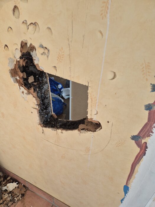 Håltagen vägg med två plyfaskivor och svart pappersmaterial emellan, visar del av äldre yttervägg i fritidshus från 1964.