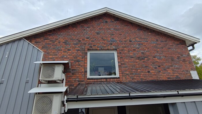 Tegelvägg med ett nyinstallerat fönster, flankerat av två luftkonditioneringsenheter, del av en husfasad under renovering.