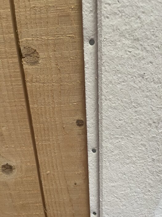 Träpanel intill vit gipsskiva, fäst med spik.