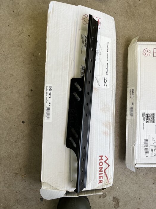 Svart Monier nockräcke på originalkartong, i varmgarage, omgiven av verktyg och andra förpackningar.