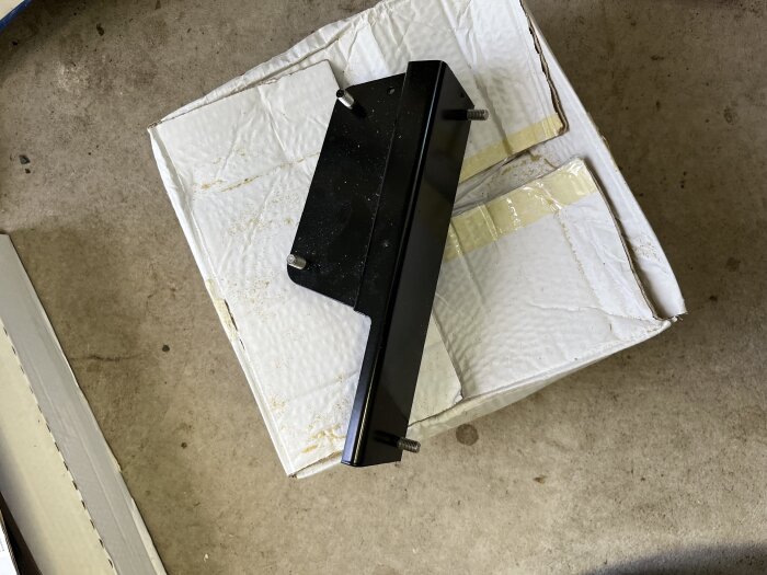 Svart konsolfäste ovanpå en vit, lite dammig kartong i ett garage.