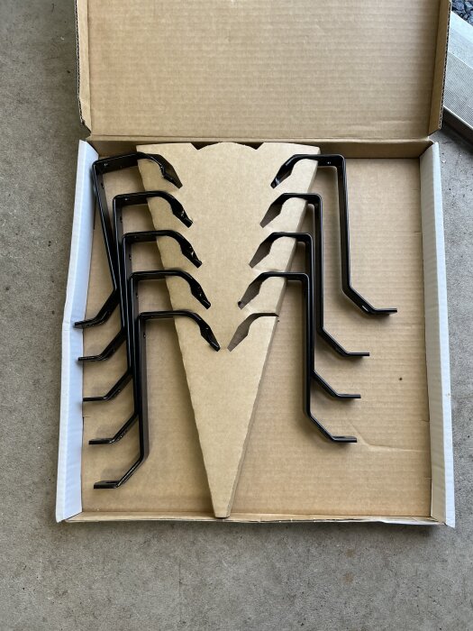 Svarta konsolbyglar packade i en öppen kartong placerad på ett betonggolv.