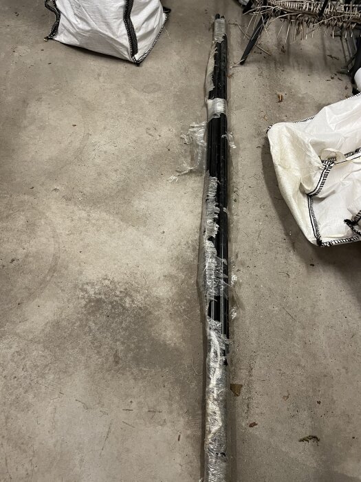 Oanvända nockräcken i plastförpackning på betonggolv, tillsammans med vita säckar, i ett varmgarage.