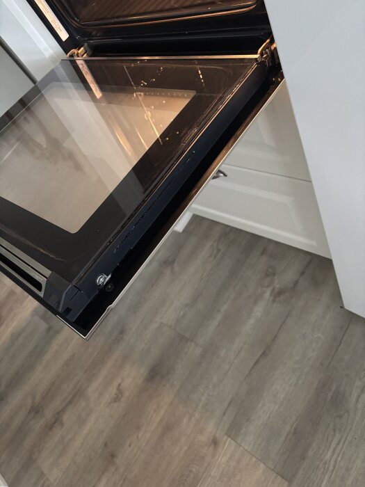 Ugn med öppen lucka i ett kök med ljus trägolv.