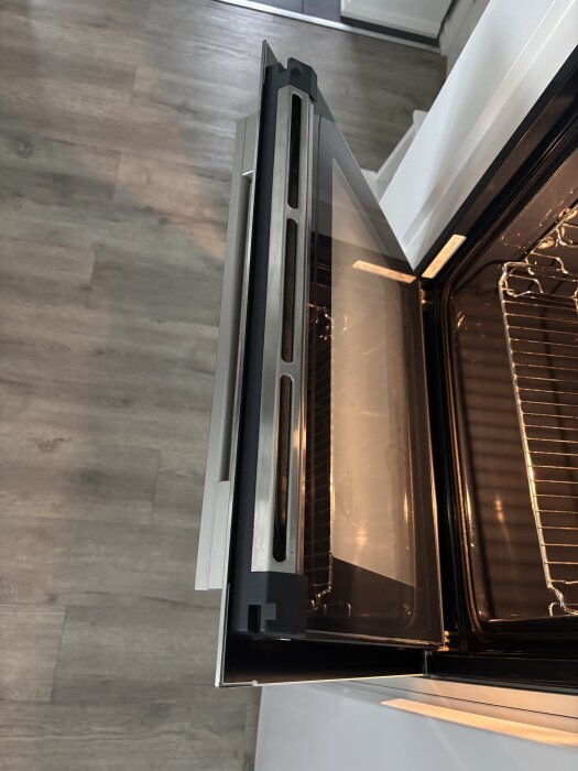 Öppen ugnslucka i ett modernt kök med trägolv.