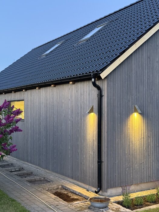 Renoverat hus med ny fasad och tak, utrustat med takfönster och belysning vid takfoten. Asfaltshingel och fasadbelysning synliga.