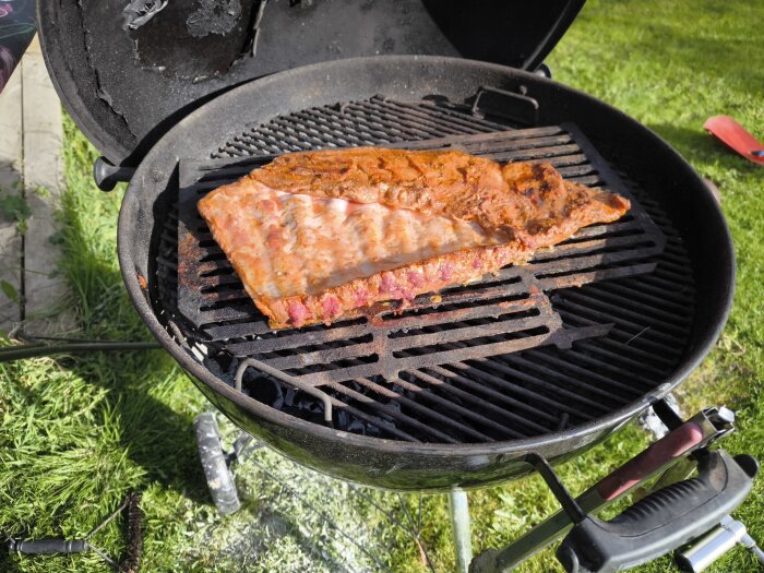 Sida av revbensspjäll grillas på en svart kolgrill utomhus i solsken.