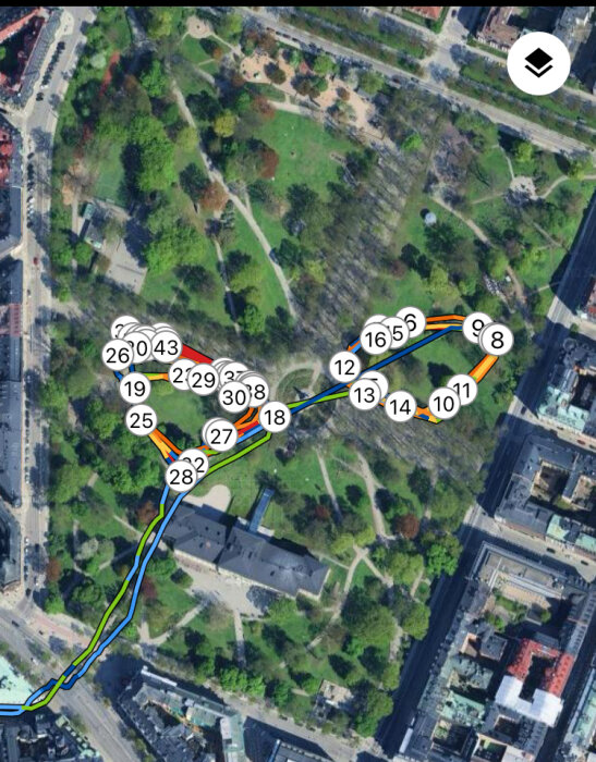 Satellitbild av en park i en stad med gångstigar och träd, markerad med numrerade punkter kopplade av färgade linjer.