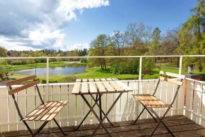 Balkong med bord och stolar, utsikt över en sjö och grönt landskap under blå himmel med moln.