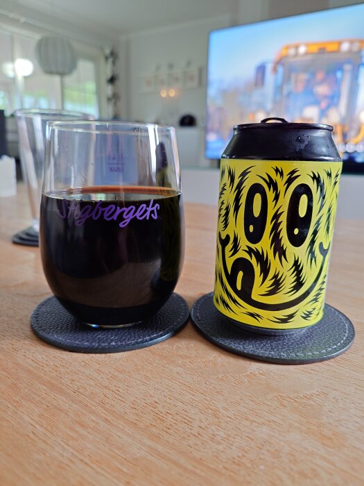 Ett glas mörk dryck märkt Stigbergets bredvid en färgglad Omnipollo Noa Bourbon Barrel 2023 Coconut can på ett bord.