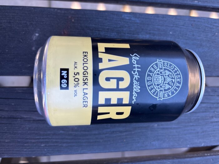 Ekologisk lagerburk från Slottskällans Bryggeri med 5% alkoholhalt, svart och gul etikett, ligger på ett bord.