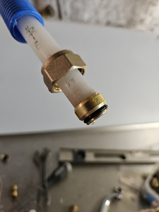 PEX-rör med blå skyddshylsa och metallhalvkoppling, ligger på en rostfri yta med verktyg i bakgrunden.
