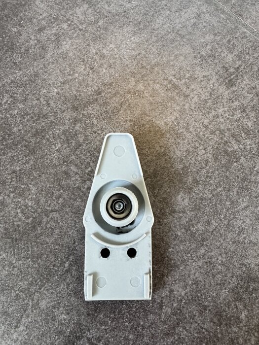 En lagad vit plastdel med hjul och hål, placerad på ett grått underlag, enligt tidigare förslag med lim.