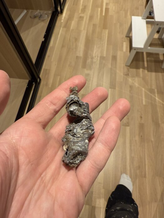 En hand håller en klump av torkat flytspackel eller betongliknande material som orsakade ett stopp i ett rör.