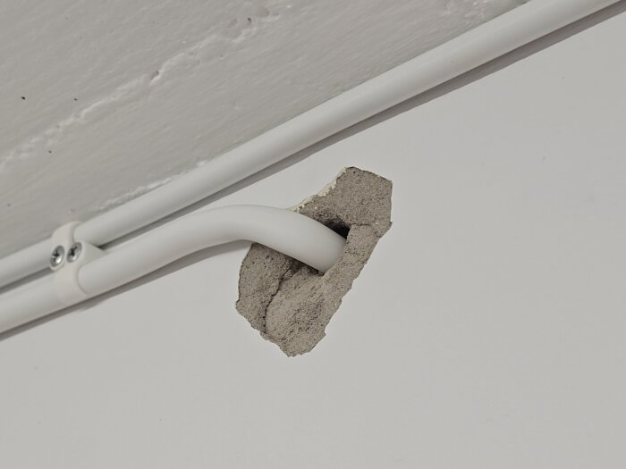 Borrat eluttag i yttervägg med synlig skada i putsen, kabel genom väggen och fastsatt med klammer.