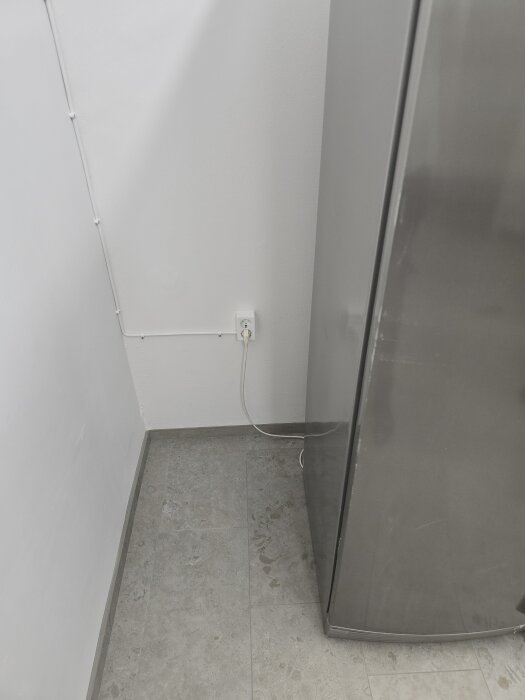 Grå frys ansluten till eluttag i renoverat maskinrum med vita väggar och klinkergolv.