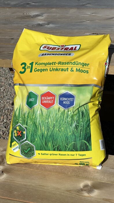 Gul förpackning med Substral 3-i-1 gräsgödsel för bekämpning av ogräs och mossa, ligger på ett bord utomhus.