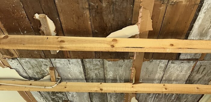 Slitet träbrädtak med mellanrum efter rivning, träreglar synliga och vissa områden med skadad yta och smuts.