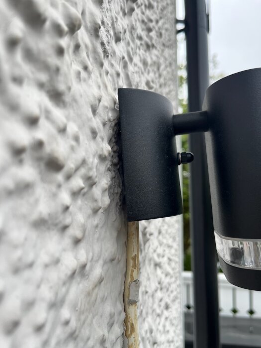 Svart lampa monterad på ojämn reveterad fasad med synlig gul kabel under, utmaning i att installera jämnt med tanke på kabeln och fasadens struktur.