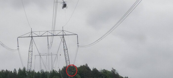 Helikopterinspektion av högspänningsledningar, person hängande i rep under helikoptern.