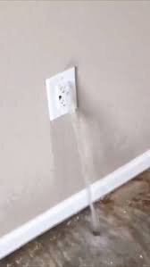 Vatten strömmar ut ur ett eluttag mot en ljus vägg och golvsockel.