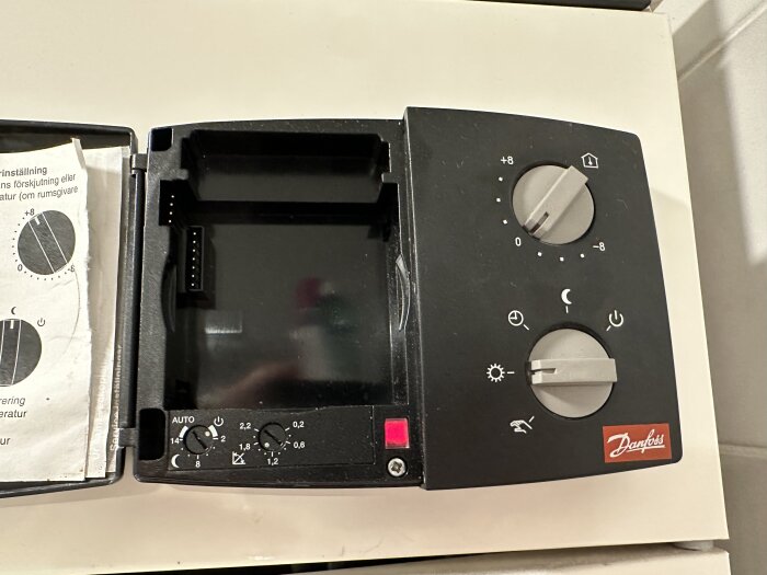 Danfoss ECL 100M fjärrvärme regulator med vridknappar för temperaturinställning och symboler för olika lägen, inklusive sol- och måne-symboler.