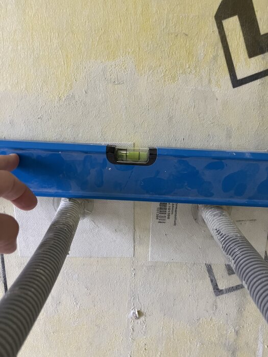 Vattenpass ovanför två synliga rör i vägg. Ett finger pekar mot vattenpasset, vilket visar att rören är ojämnt installerade.
