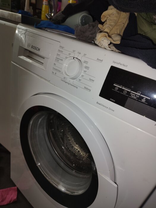En Bosch tvättmaskin med kläder ovanpå, synlig panel med inställningar och dörr till trumman som är stängd.