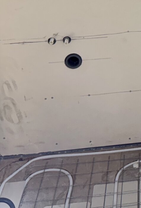 Vägg med två synliga rörkopplingar och en svart rund öppning, omgiven av byggmaterial och ritningar på ytan, del av rörinstallation.