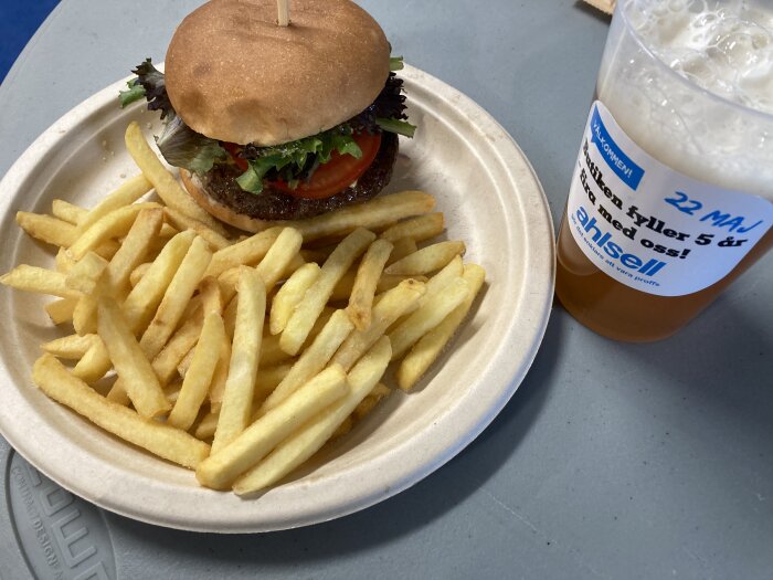 Älgburgare med pommes på papptallrik bredvid en plastmugg med öl från Fenix Brewery.