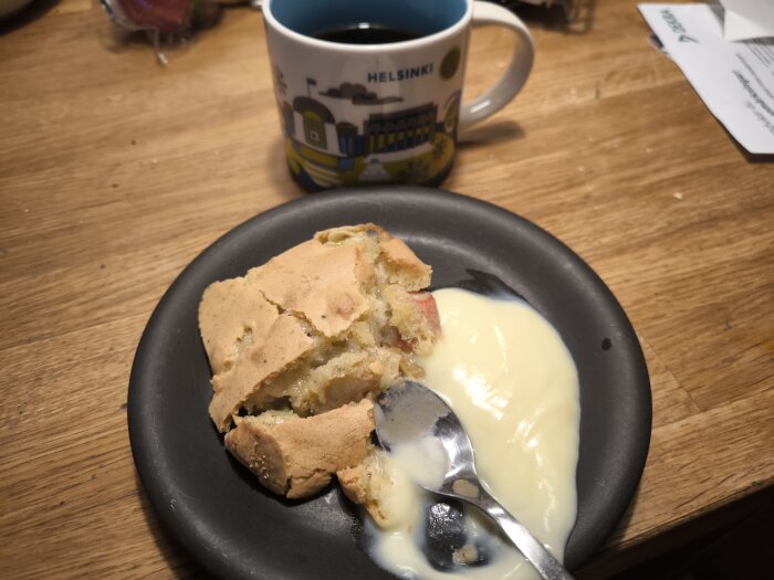 En bit rabarberpaj med vaniljsås på en svart tallrik, bredvid en kopp kaffe med texten "Helsinki".