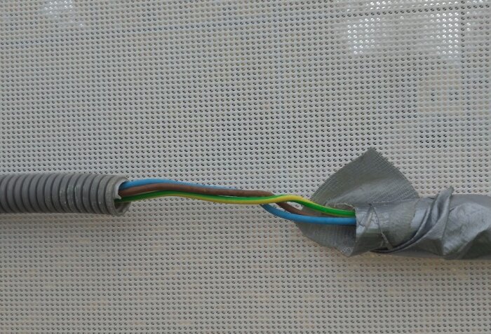 Elektriska kablar provisoriskt isolerade med silvertejp, placerade mot ett vitt insynsskydd vid en byggarbetsplats.
