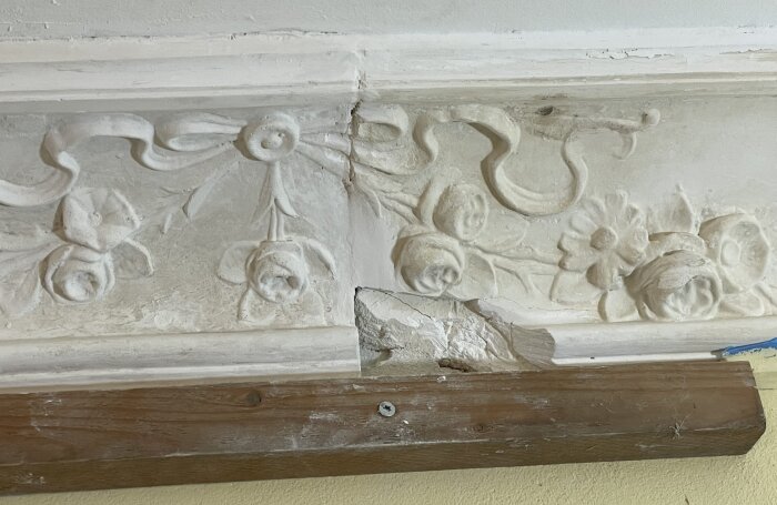 Stuckaturdetalj med blommönster, delvis reparerad. Gipsspricka synlig, omgiven av dekorativa rosor och blommor på en vit bakgrund.