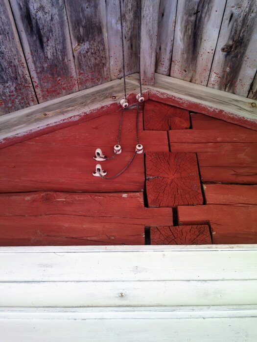 Röd trävägg med gammaldags elinstallation bestående av porslinsisolatorer och synliga kablar mot vägg i Norbottenshemman.