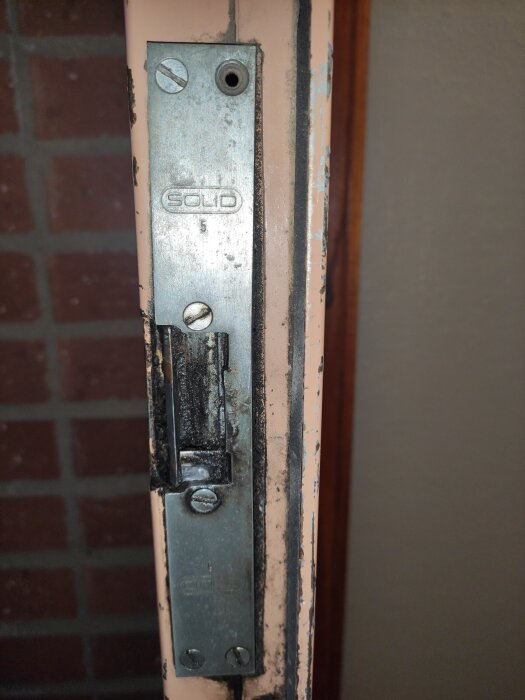 Elslutbleck fastskruvat i dörrkarm med logotypen "SOLID", visas i närbild, möjligtvis defekt då dörren alltid är låst.